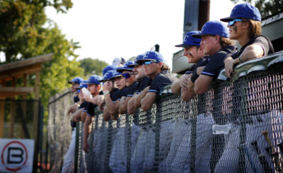 Line of baseball players waiting by a fence to play